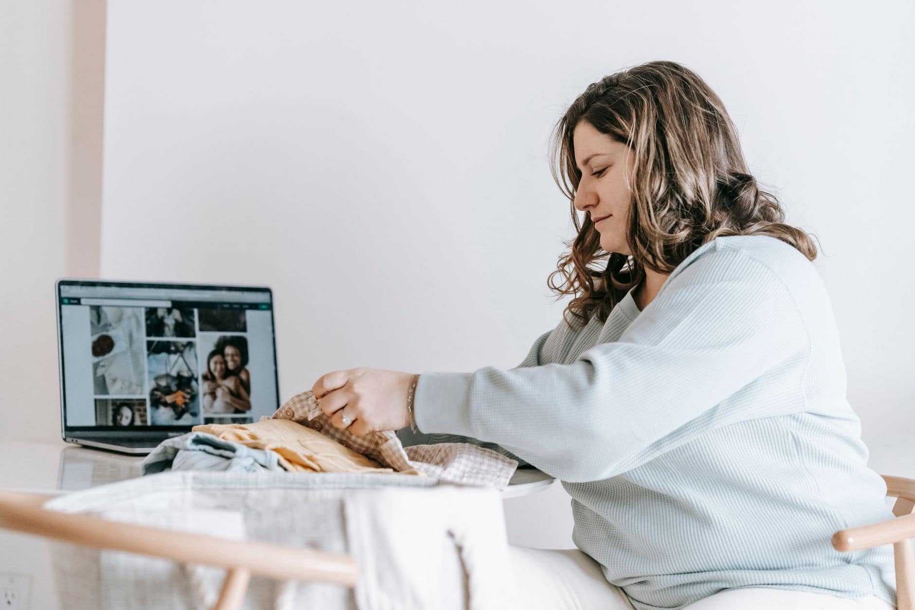 woman folding baby clothes near laptop