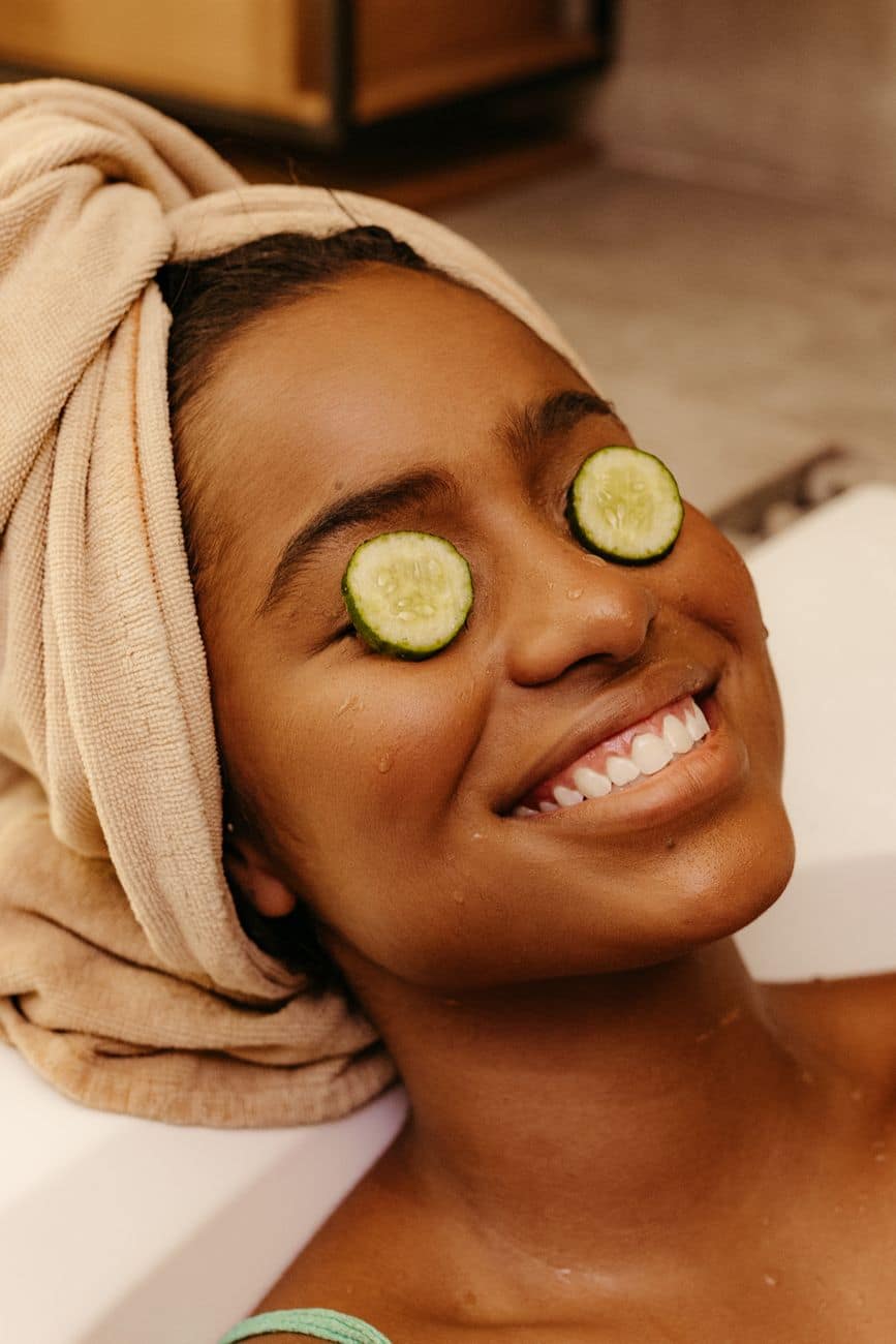 woman with cucumber slices on her eyes lying in a bathtub